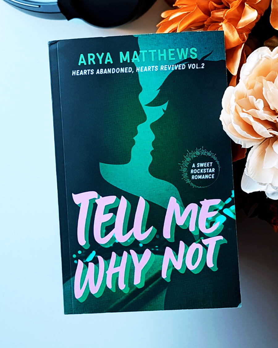 a photo of a book by Arya Matthews Tell Me Why Not with roses and headphones